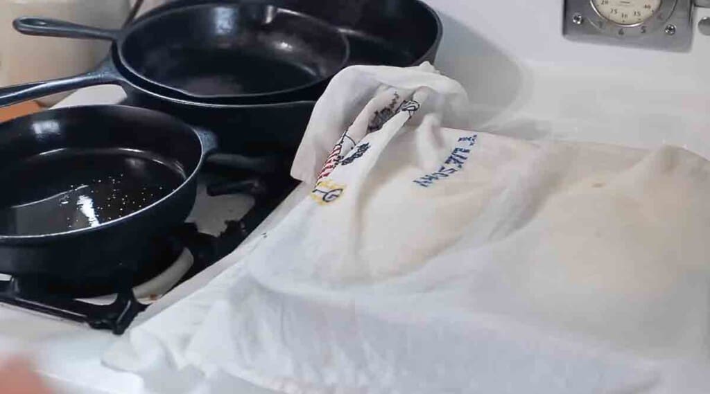 tea towel over two loaves of sourdough sandwich bread on a white vintage stove with cast iron skillets to the left