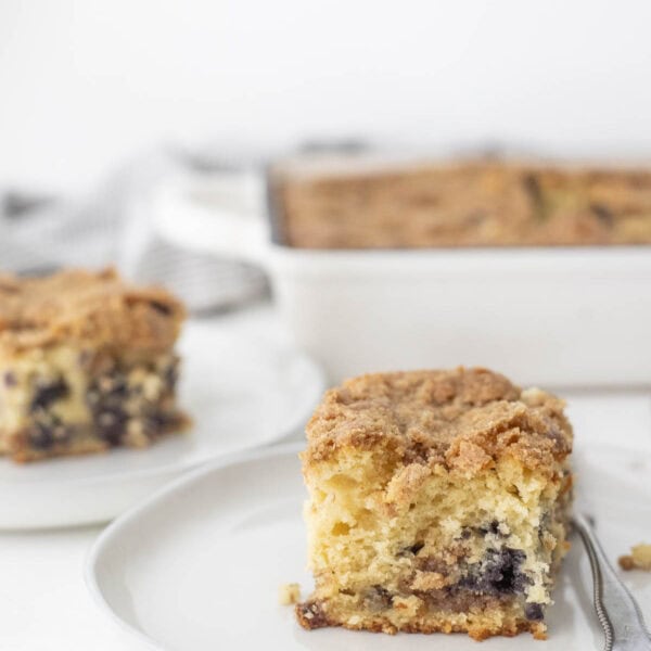 a slice of sourdough blueberry coffee cake on a plate with more coffee cake in the background.