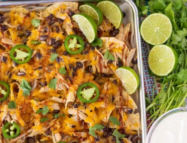 Baking sheet with Pulled Pork Nachos and sliced limes. Pico, guacamole and sour cream on the side.