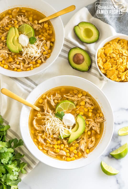 a bowl of chicken tortilla soup topped with lime, sour cream, cheese, and avocado