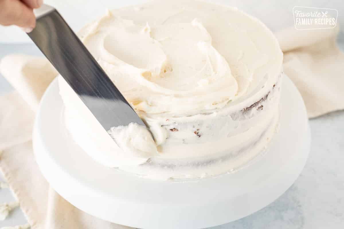 Spreading cream cheese frosting on stacked carrot cakes.