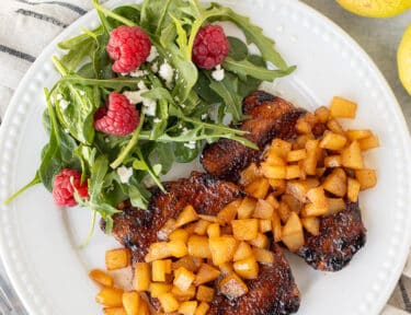 Two Grilled Pork Chops with Spiced Pears on a plate with a green salad.