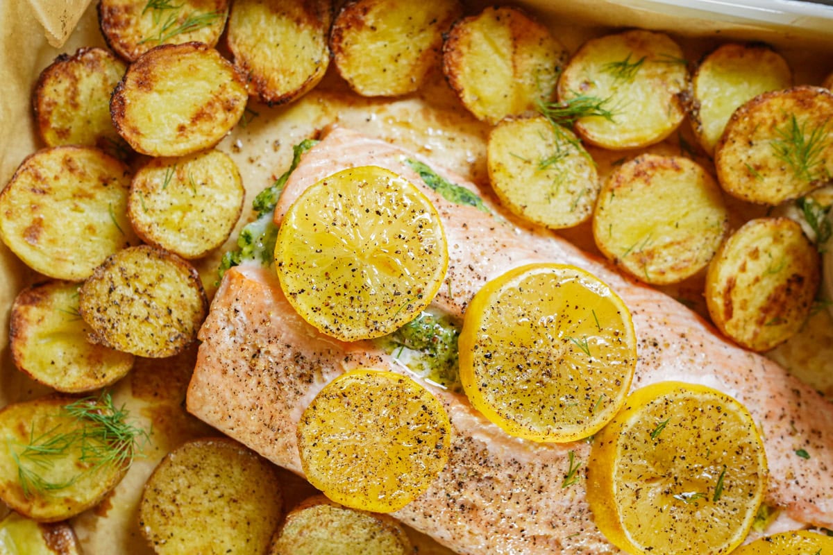 A salmon fillet topped with lemon slices, rests on a bed of roasted potatoes