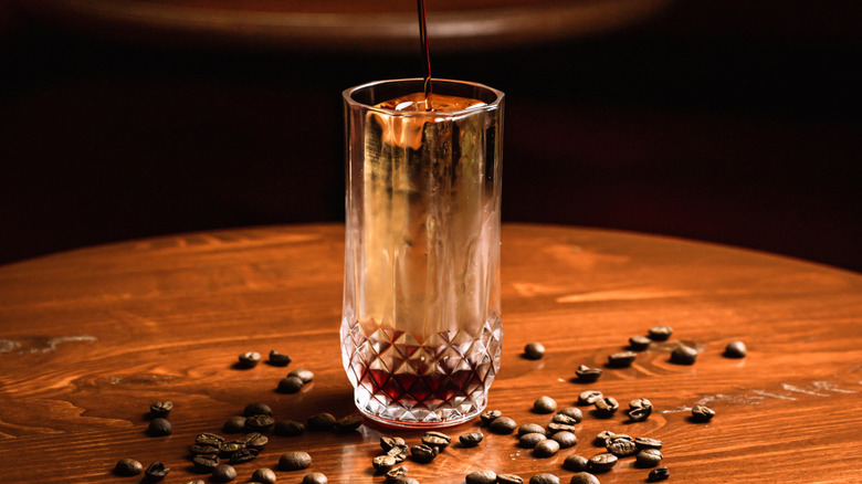 Pouring a cocktail into a glass with a Collins spear in it.