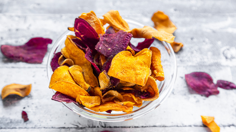 A clear bowl of orange and purple veggie chips sits on a gray counter