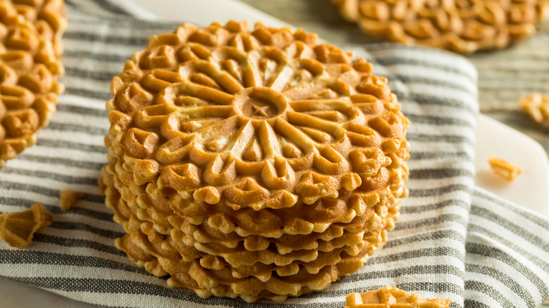 Stack of golden, round pizzelle cookies on striped kitchen towel