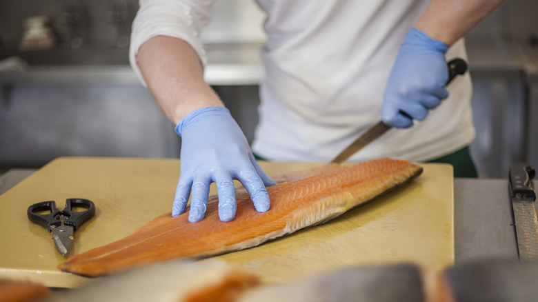 A chef trimming a side of salmon in his kitchen