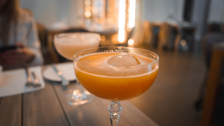 Close up of an orange cocktail with a sphere of ice sitting on a table