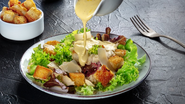 creamy salad dressing pouring onto chicken caesar salad