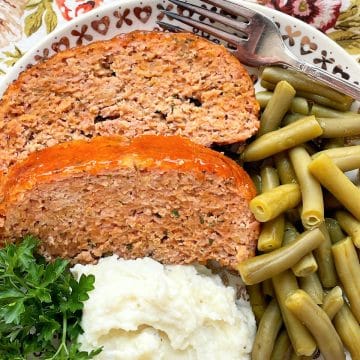 two slices of apricot glazed ham loaf on a plate with mashed potatoes and green beans