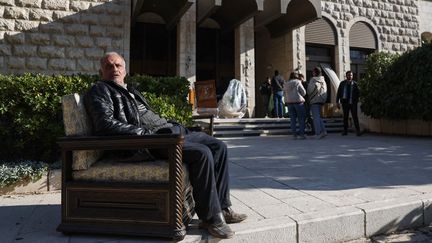 Un homme assis dans un fauteuil à l'extérieur du palais présidentiel du président syrien déchu Bachar al-Assad, à Damas (Syrie), le 8 décembre 2024. (OMAR HAJ KADOUR / AFP)