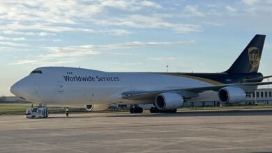 A brown-tail UPS jumbo jet freighter is towed by a tug at an airport on a clear day.