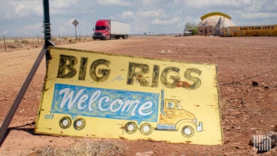 A sign saying "Big Rigs Welcome" in front of a dirt parking lot