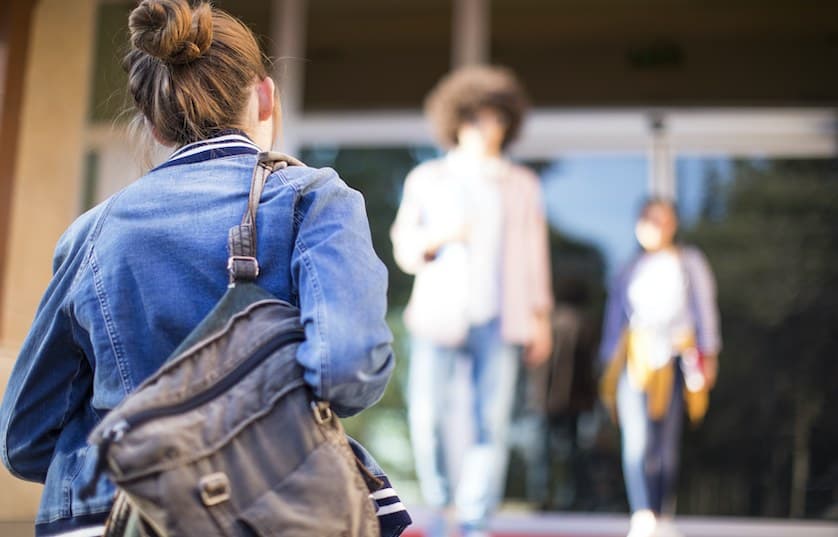 person with jean jacket and backpack walking toward entrance of building