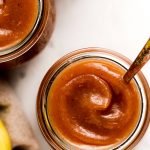 Apple butter in jars with apples to the side.