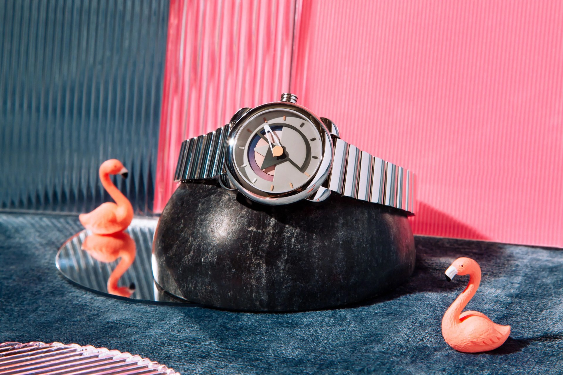 a watch on a watch stand next to miniature pink flamingos