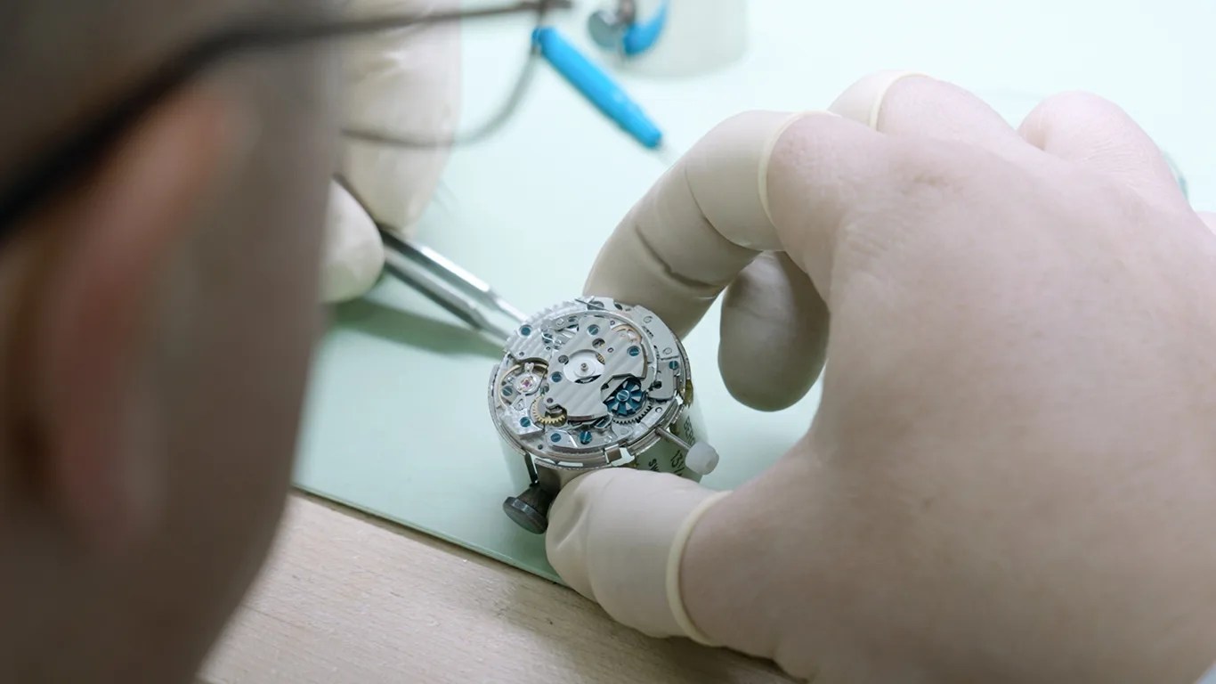 a closeup of a man repairing a watch movement from watchcheck