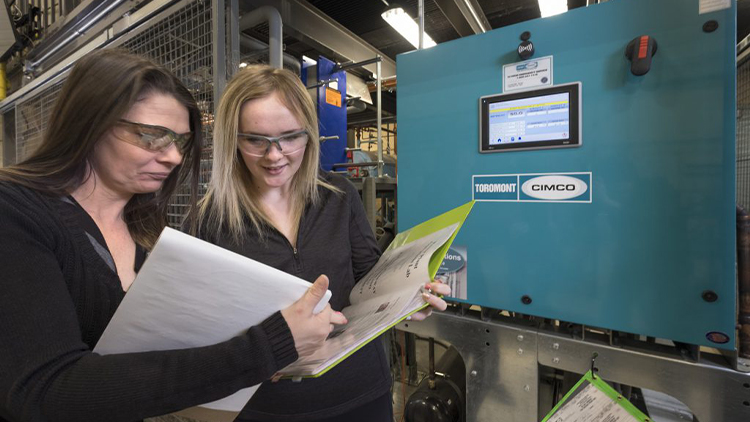 two female students wearing safety goggles and reading a binder in skilled trades lab