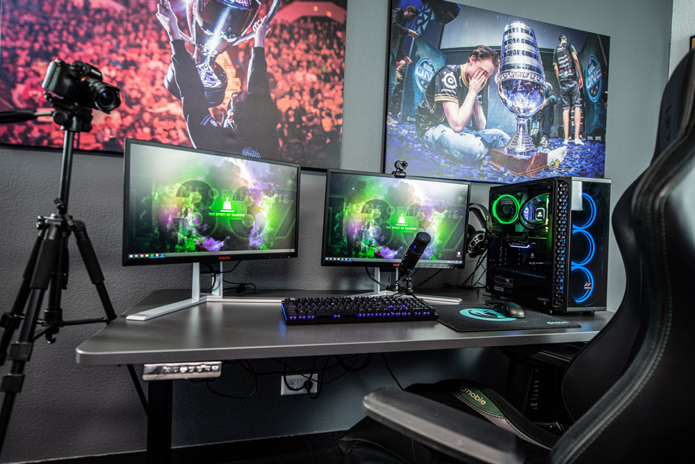 Desk setup featuring computer monitors, a computer tower, mouse, keyboard, camera and microphone, used by a gamer and streamer