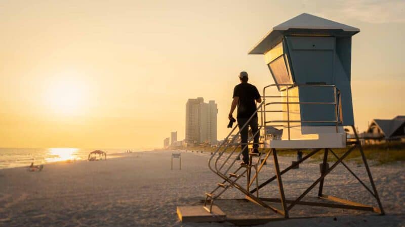 Man with a camera standing on the beach in PCB Florida watching th yellow sunset - Best things to do in Panama City Beach