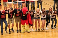 Football players and cheerleaders doing a cheer on the gym floor