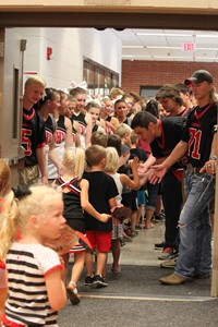 Elementary students walking through tunnel of high school football players