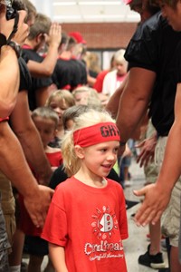 Elementary student walking through tunnel of high school football players