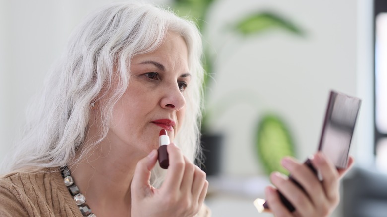 Woman with gray hair applying red lipstick