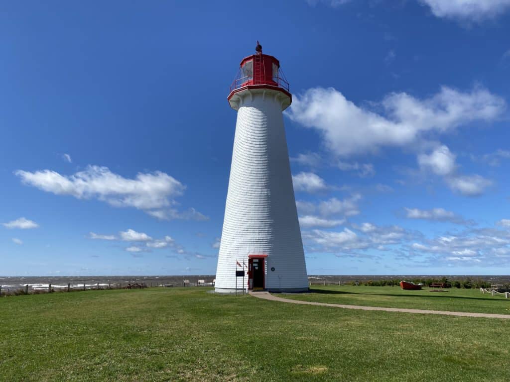 White with red trim Point Prim Lighthouse in PEI with blue sky and fluffy white clouds.