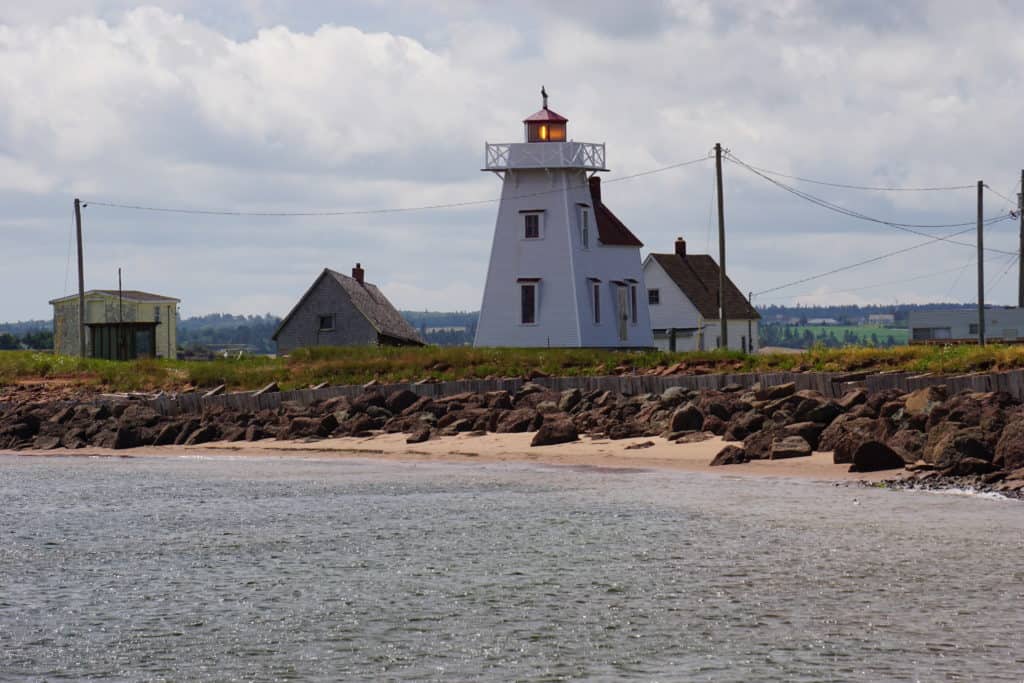 North Rustico Lighthouse and outbuildings at rocky shore of ocean.