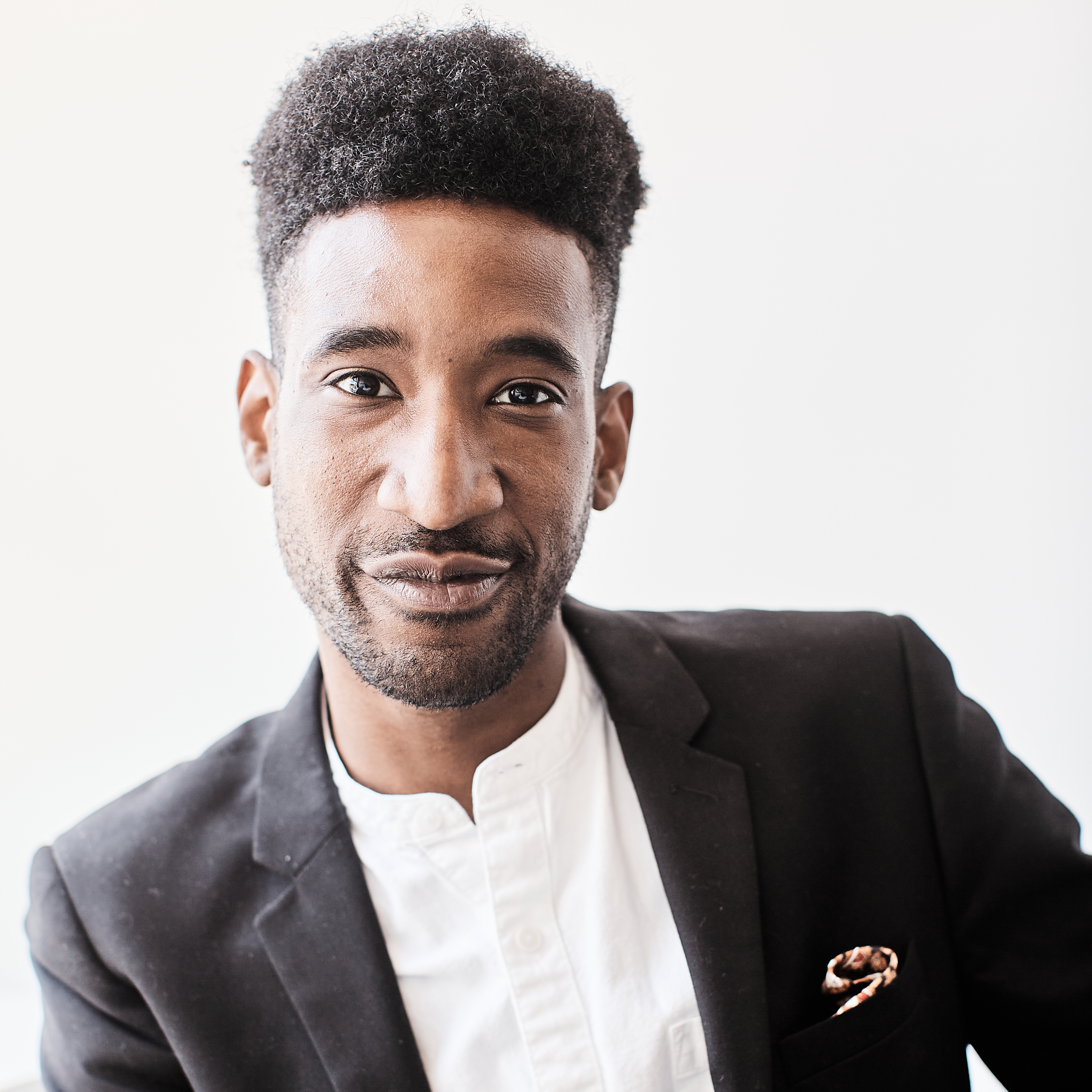 Photograph of a Black man with short hair who is wearing a suit smiling towards camera.