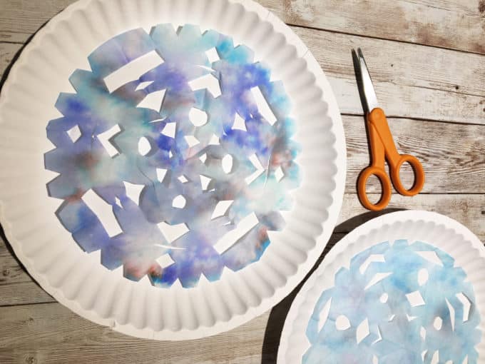 Blue dyed coffee filter cut to look like a snowflake on a white paper plate