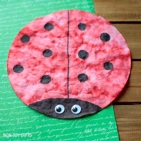 Red with black dots coffee filter in shape of ladybug on green background.