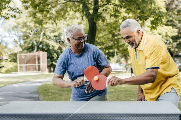 Two Seniors Playing Ping Pong Together Outside During The Spring.