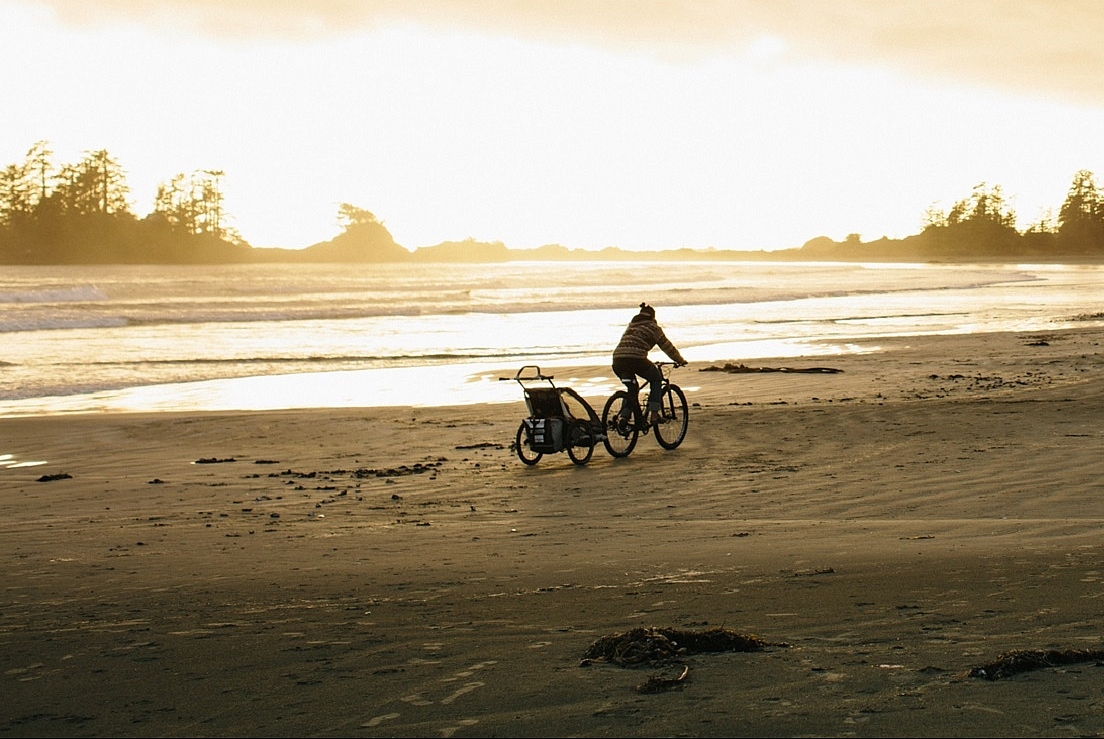 A person on a bike pulls a trailer long the beach.