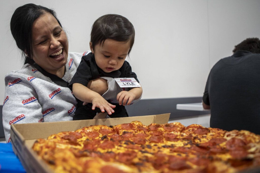 Family friend Nian Enriquez, left, smiles as Carlisle “Lyle” Sarmiento, right, reaches for a pizza during his first birthday party at Costco in Lake Stevens on Friday, May 31, 2024. (Annie Barker / The Herald)
