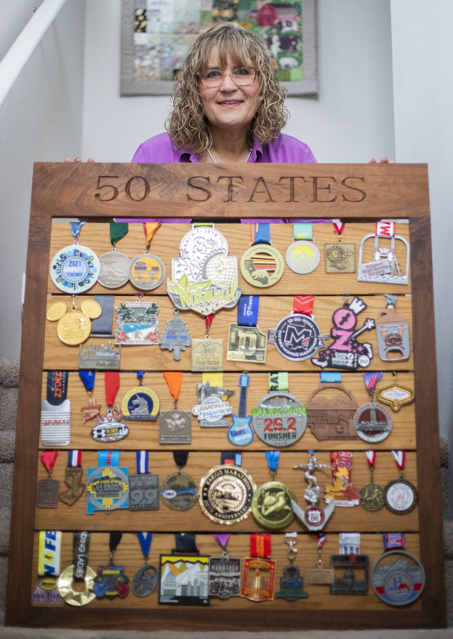 Robin Cain with 50 of her marathon medals hanging on a display board she made with her father on Thursday, Jan. 2, 2025 in Lake Stevens, Washington. (Olivia Vanni / The Herald)