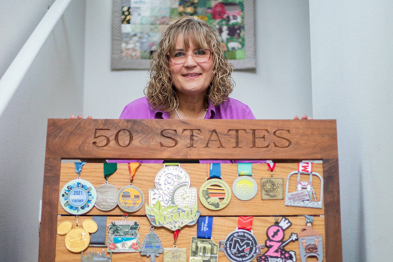 Robin Cain with 50 of her marathon medals hanging on a display board she made with her father on Thursday, Jan. 2, 2025 in Lake Stevens, Washington. (Olivia Vanni / The Herald)