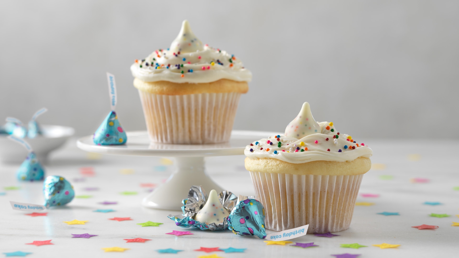 vanilla cupcakes topped with vanilla frosting, sprinkles, and hersheys kisses birthday cake candies