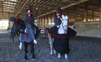 Two horses and two riders. One horse is dressed as a magician. One horse is dressed as a bunny coming out of a top hat. Both riders are dressed as magicians.