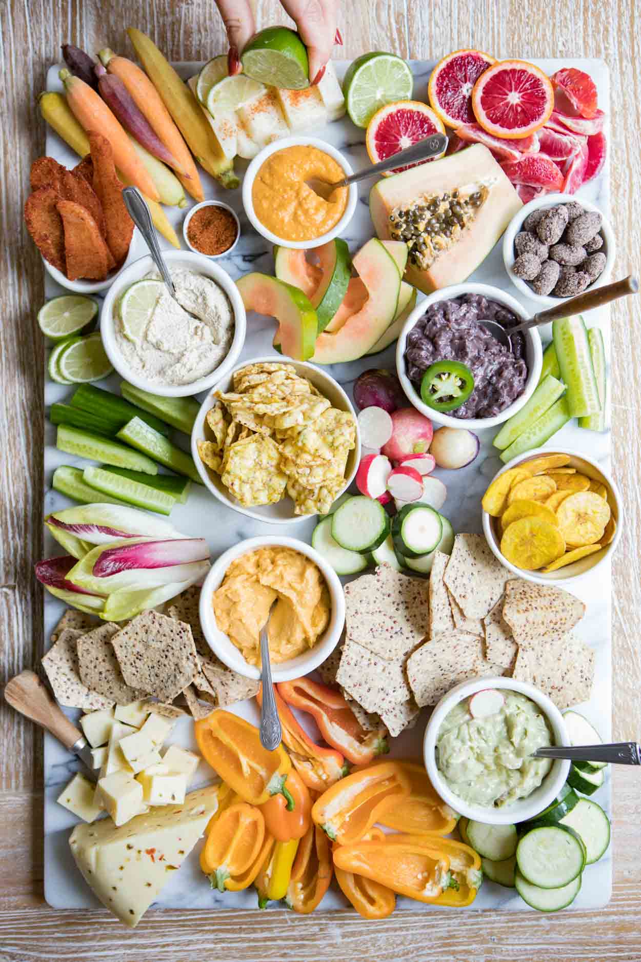 cucumbers, peppers, chips, dips and various other fruits and veggies on a marble slab for a crudite platter