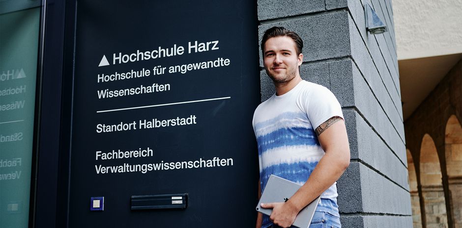 Ein Student des Public Management lehnt am Eingang des Fachbereichs Verwaltungswissenschaften.