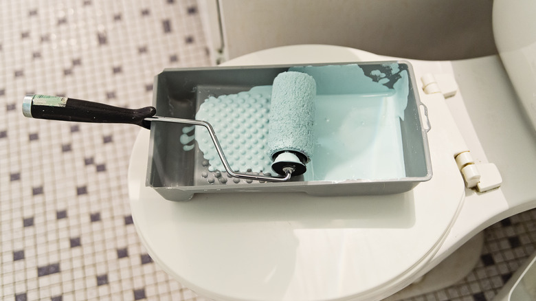 Roller of paint in bathroom on top of toilet