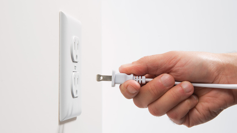 Person's hand preparing to plug a cord into an electrical receptacle