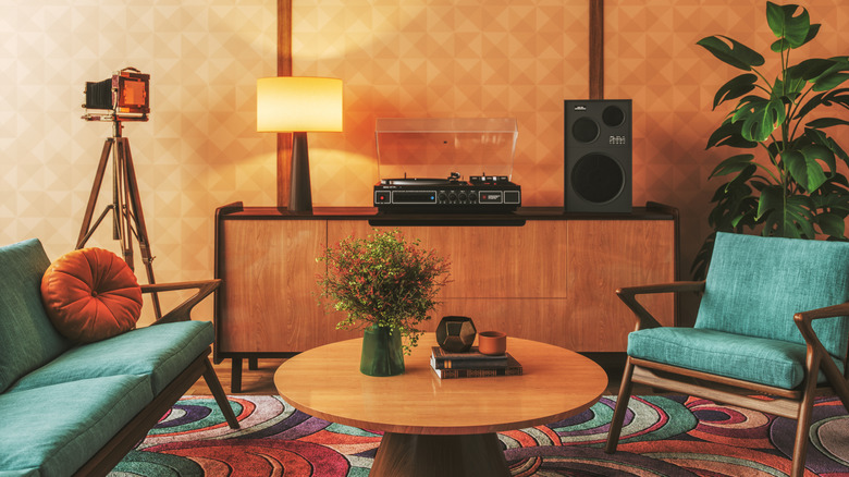 A 1960s style living room with mid-century furniture, a colorful swirl-patterned rug, an antique camera on a tri-pod and a record player.