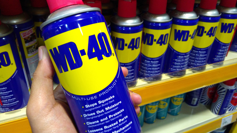 hand holding a can of WD-40 in a store aisle with more of the same product on the shelf behind it