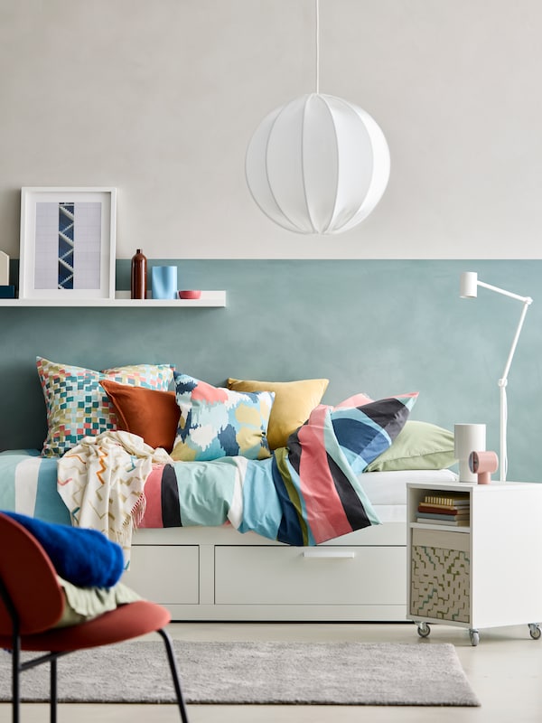 A white BRIMNES day-bed with SVALSTJÄRTAR duvet cover and pillow cases. A VIHALS bedside table and a GÄVLE chair in front.