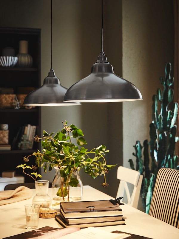 Two ANKARSPEL pendant lamps hang above a white INGATORP extendable table with books and vases on top of it.