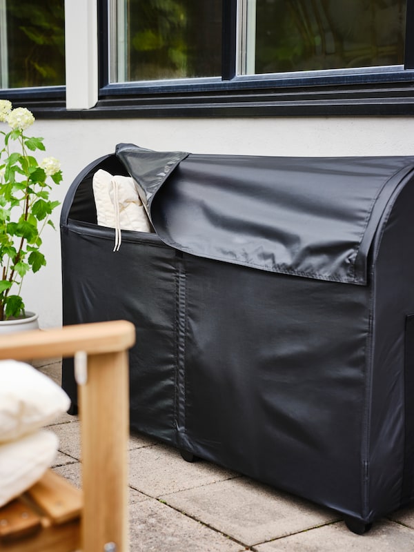 A TOSTERÖ outdoor storage box standing on a tiled floor. One corner is lifted, showing some KUDDARNA chair cushions inside.