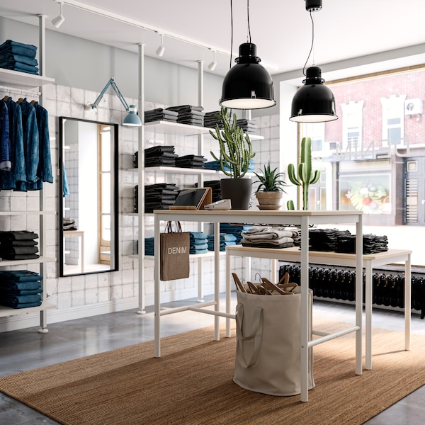 A light, airy store interior with a LOHALS rug and denim garments arranged in white ELVARLI storage combinations.